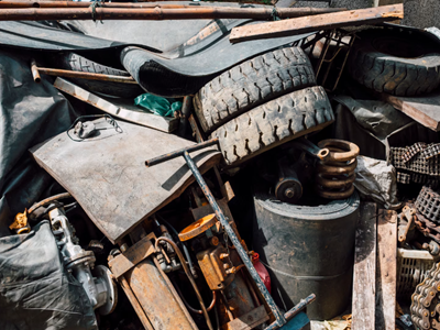 A large pile of industrial scrap waste including old rubber tires, rusted vehicle parts, metal chains, and heavy springs.